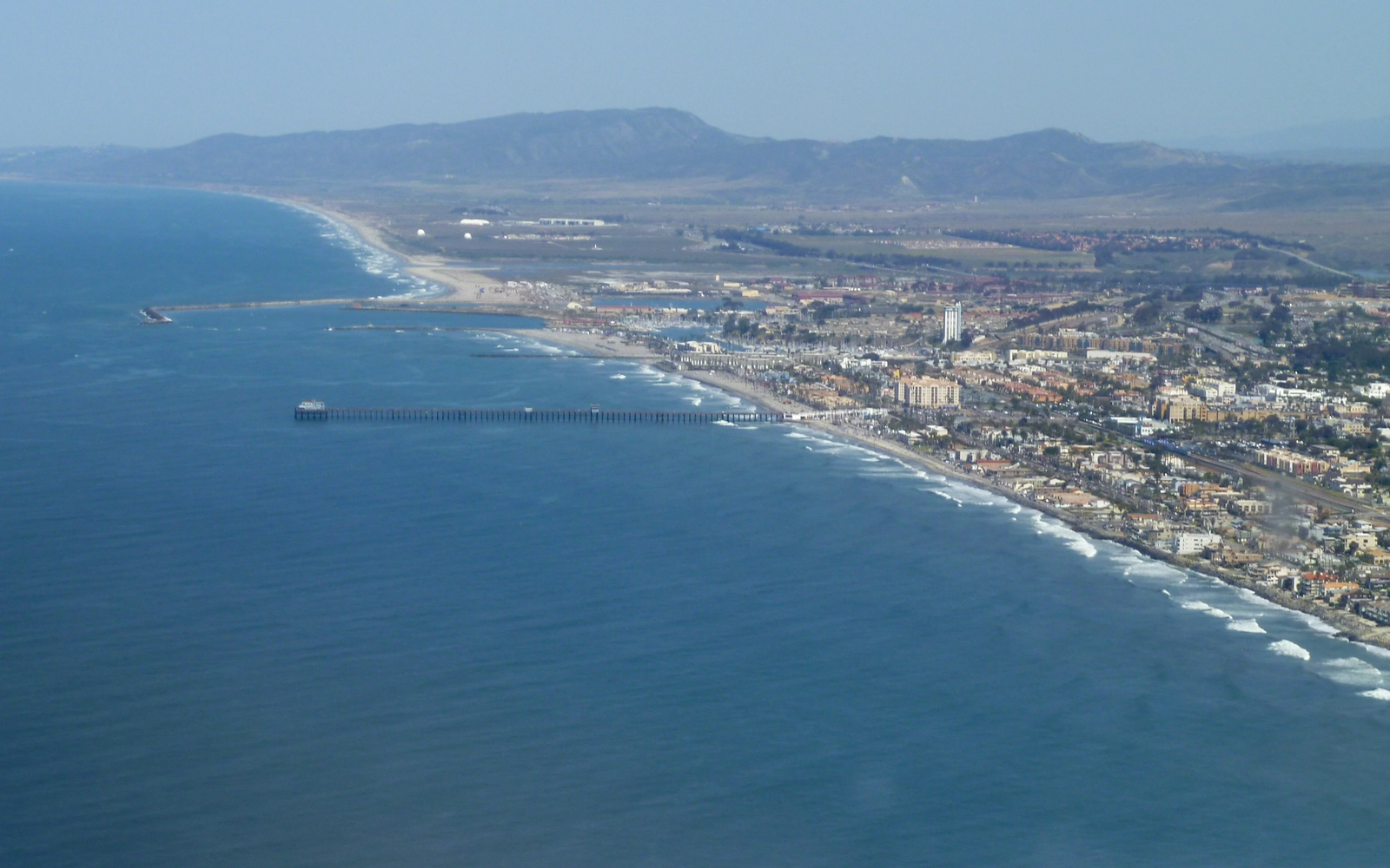 Aerial view of the Oceanside shoreline with the municipal pier reaching into the Pacific and the harbor to the north